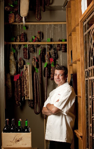 Chef Spencer Minch of Emeril's Delmonico stands among beautiful aged meats and wines.