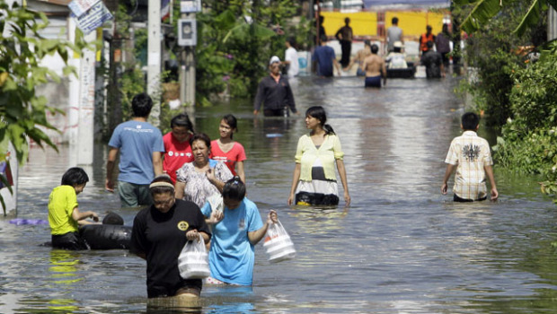 People wade through floodwaters in Bangkok, Thailand, 25 October 2011. Thailand's flood crisis deepened Tuesday after floodwaters breached barriers protecting Bangkok's second airport, effectively forcing a halt to commercial flights there after airlines using it suspended operations. Sakchai Lalit / AP Photo