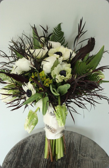 White Ranunculus, Anemone and Parrot Tulips are surrounded by feathery Agonis and Ferns with Black feather accents. blush floral design White Ranunculus, Anemone and Parrot Tulips are surrounded by feathery Agonis and Ferns with Black feather accents. blush floral design