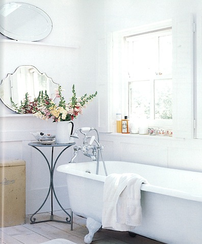A beautiful collection of mirrors on the wall illuminates this already bright and airy all-white bathroom.  Touches of color can be added with flowers and colorful jars of shampoo and bath oil.