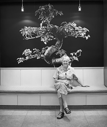 Beatrice Dryer sits in the lobby of the Martha Stewart Center for living at Mount Sinai Medical Center. Behind her, a photograph of a bonsai tree, a symbol of longevity, strength, and beauty.
Photograph by John Huba