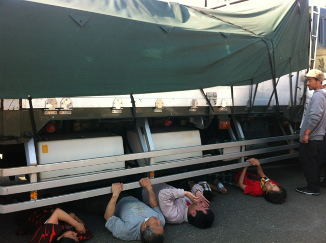 Protesters in Kitakyushu City lay under a truck carrying radioactive debris that officials have decided to incinerate, 21 May 2012. asat8 via ex-skf.blogspot.com