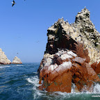 The blue sea washes the white guano exposing the red rock.
