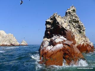 The blue sea washes the white guano exposing the red rock.