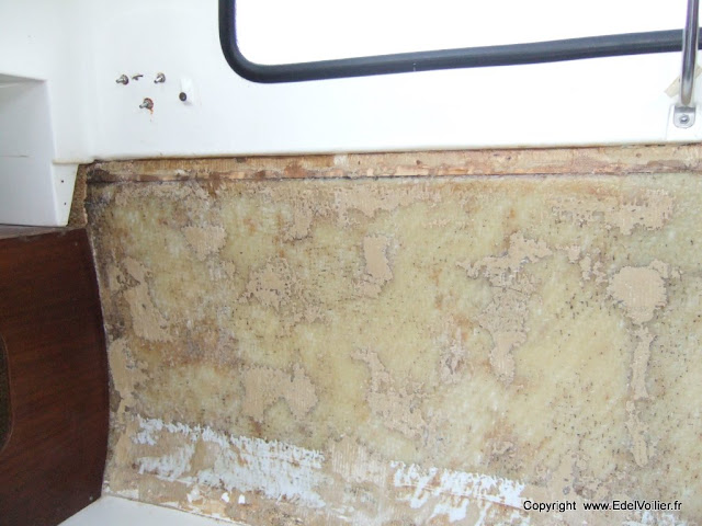 Paroi de la coque dans le carre. La moquette à été arrachée, la colle enlevée au ciseau à bois puis coque poncée à la brosse en fer montée sur perceuse. Maintenant la paroi est prête pour recevoir une couche de mastic polyester pour égaliser