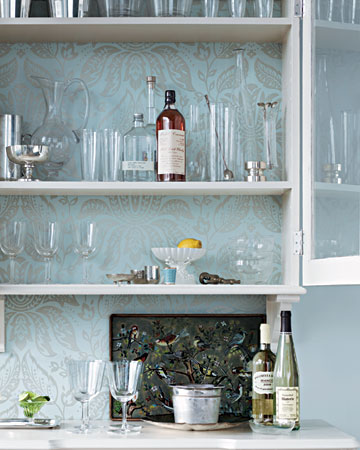 Give her bar a stylish update. Two disparate pieces -- a cabinet and a desk -- become one, thanks to the clever use of wallpaper. The sophisticated pattern makes a beautiful backdrop for a collection of glasses. To get this look, adhere a wallpaper panel above the desk and mount the cabinet. Remove cabinet shelves, and line the back with wallpaper; be sure to line up the center of the cabinet panel with the center of the wall panel below (marthastewart.com) Give her bar a stylish update. Two disparate pieces -- a cabinet and a desk -- become one, thanks to the clever use of wallpaper. The sophisticated pattern makes a beautiful backdrop for a collection of glasses. To get this look, adhere a wallpaper panel above the desk and mount the cabinet. Remove cabinet shelves, and line the back with wallpaper; be sure to line up the center of the cabinet panel with the center of the wall panel below (marthastewart.com)