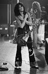 Led Zeppelin guitarist Jimmy Page holds his arms across his chest during a concert. Singer Robert Plant stands beyond. ca. 1973-1978 USA