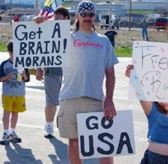 c0 This image speaks for itself. A man is holding signs that say "GO USA" and "Get A BRAIN! MORANS"