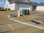 Aftermath in the front lawn: cover for the cable box blew away, someone's siding, A/C compressor on its side, and someone's dead Christmas tree by my garage.