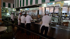 Waitresses line up to fill cups of coffee and pick up dishes of beignets on cafeteria trays.