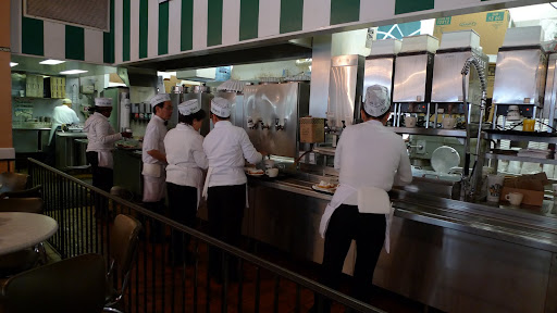 Waitresses line up to fill cups of coffee and pick up dishes of beignets on cafeteria trays.