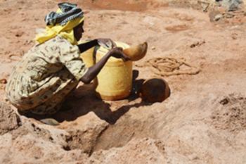 In southern Kenya, a woman uses a gourd to scoop water from a dry riverbed. During droughts, many women walk hours to find water. Photo: Laura Sheahen / Caritas