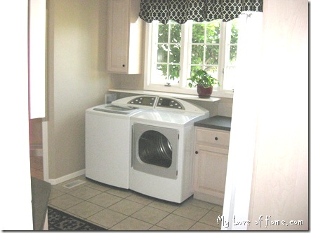 white washer dryer, beigh tile, beige walls, white wood work, black curtains, red pot