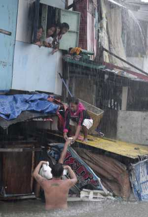 A man gives food to people staying in flooded homes in Quezon City, north of Manila, Philippines, on 7 August 2012. Emergency crews were scrambling to evacuate tens of thousands of residents. Associated Press