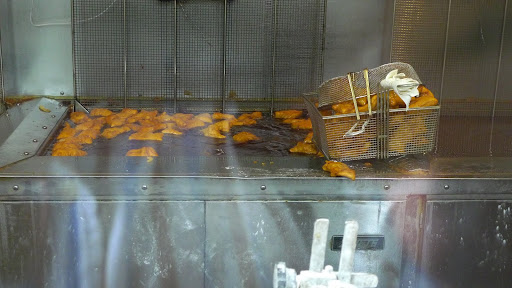 A cook transfers the dough squares to hot oil, which fries them up into puffy golden fritters.