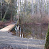 The pond features an elegant bridge connecting wooded trails.