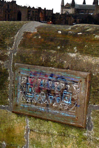 Graffitied wall-mounted plaque in Durham, with parts of the cathedral and castle visible in the background.