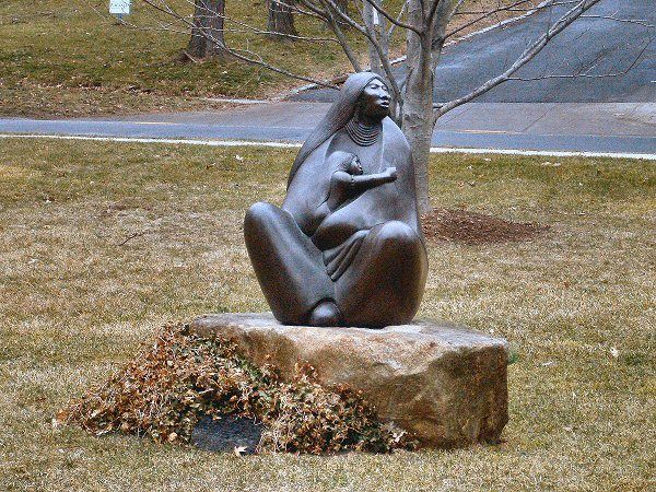 Apache sculpture of Earth Mother, woman cradling a baby, looking off to one side, singing