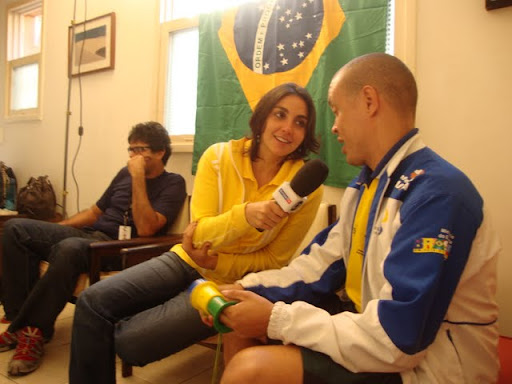 Na foto, a repórter Larissa Abbud entrevista Anderson Dias. Os dois estão sentados no sofá da sala da casa de Gabriel Mayr