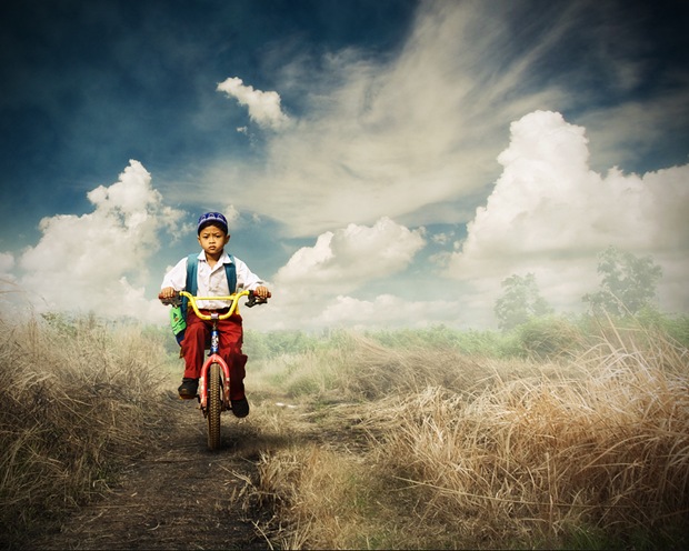 An Indonesian elementary student goes to school with a bike through a barren land. An Indonesian elementary student goes to school with a bike through a barren land.