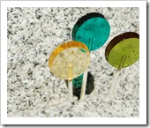 gold, teal, and avocado green lollipops on a granite bench