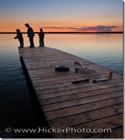A Father with his two sons fishing at the end of a wharf on Lake Audy at sunset, Riding Mountain National Park, Manitoba, Canada.