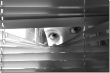 Young female looking through window blinds at night.(shallow depth of field)