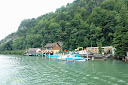 Piles protecting some boats on the shore of Lake Lucerne, with a green tree covered hill as the background - Thumbnail