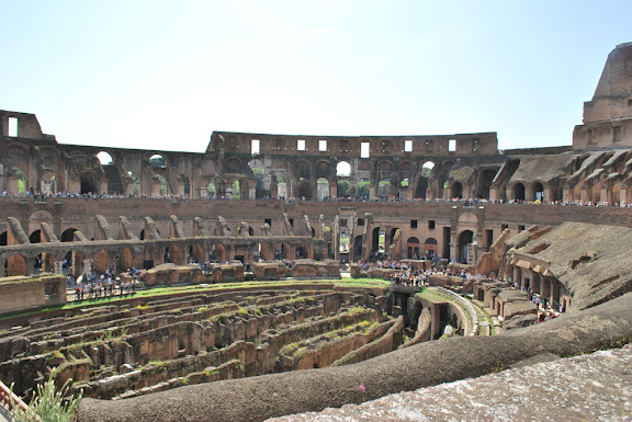 a large circular structure with many arches with Colosseum in the background