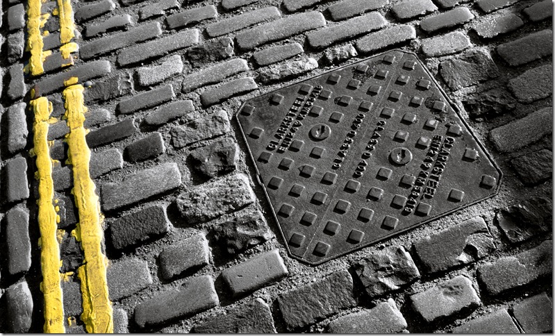 cobbled street with drain cover and painted double  yellow lines