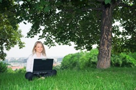 Beautiful young girl sitting in a meadow and working with her laptop computer [János Gehring em www.123rf.com]