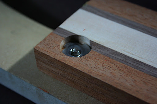 This mock-up shows the anatomy of a Decibel Guitars bolt-on neck joint. Threaded T-nuts are inserted underneath the fretboard. They are threaded to receive a connector bolt, and have a 3/4" flange and steel prongs that secure it in the wood.