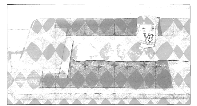  A strip of paper is aligned with the carpenter's square, and held in place with a heavy weight: in this case a can of V8 Juice.