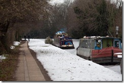 two people take a walk on the foot path, inside the boats people run their furnaces to keep warm