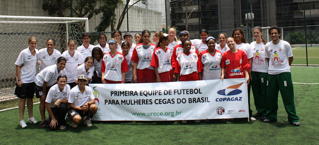 Na foto, equipe de futebol feminino da Urece pousada para foto. As jogadoras têm na mão um cartaz onde se lê "Primeira Equipe de futebol para mulheres cegas do Brasil"