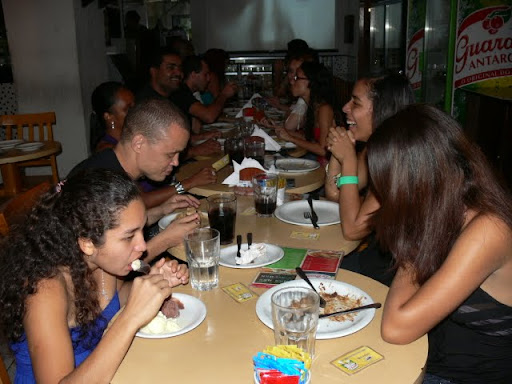 Na foto, aparece a mesa em que se vê os convidados comendo e conversando, durante comemoração do aniversário de Anderson Dias
