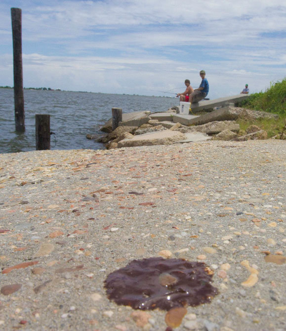 A tar ball from the Deepwater Horizon oil spill washed ashore near the Treasure Island subdivision in Lake Pontchartrain as people fish near the Rigolets in Slidell, Monday July 5, 2010. MATTHEW HINTON / THE TIMES-PICAYUNE