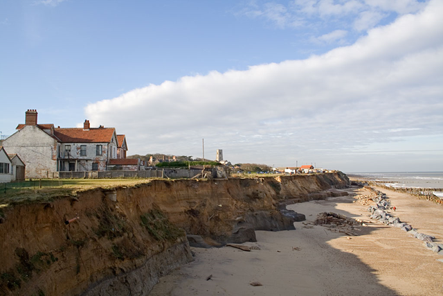 Looking north west from the end of Beach Road, Happisburgh. The soft sedimentary rock of the cliffs is seeing some of the fastest coastal erosion in Norfolk. Several houses on Beach Road have already been lost to the sea and many of those remaining are in a precarious position. Some of the 1950s sea defenses, built to protect the village from further erosion, can be seen along the beach. The tower of the 15th century St.Mary's Church can be seen in the background. Photograph &copy; Andrew Dunn, 04 November 2006 via commons.wikimedia.org