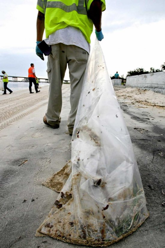A member of a clean up crews drags a trash bag full of tar balls and sand on the beach in Ocean Springs, Mississippi, USA, 28 June 2010. After oil had washes up on the inland Mississippi shoreline for the first time, the city of Ocean Springs ordered to close the beaches but later rescinded the order after it was discovered that the brown foam thought to be oil was not dangerous. EPA / DAN ANDERSON