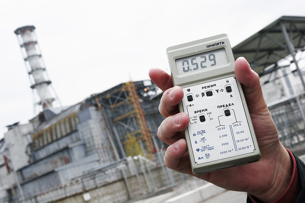 A dosimeter outside the Chernobyl Nuclear Power Plant reads the current radiation dose — 20 to 30 times higher than normal background levels. At left is the concrete 'Sarcophagus' built over destroyed reactor #4, where the meltdown occurred during a late-night safety test.  The sarcophagus leaks and is structurally unstable. Construction workers preparing foundations for a replacement 'New Safe Confinement' sometimes reach their daily dosage limits in two to three hours. Photo: Michael Forster Rothbart / afterchernobyl.com