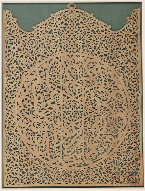 This découpage panel in the shape of a closed altar piece includes a central roundel decorated with interlacing letters whose stems form a central six-pointed star. The round inscription is difficult to decipher, and may comprise a wise saying or a verse from the Koran. In the middle of the upper arch, a round hook suggests that it was used as a wall hanging.