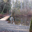 The pond features an elegant bridge connecting wooded trails.