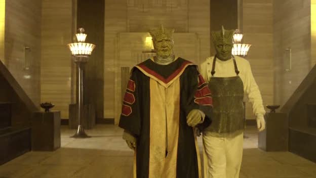 Eldane wearing robes with chevrony things on the sleeves and a colored panel down the front