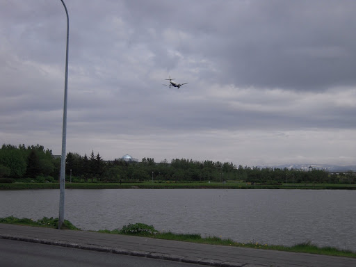 A plane landing at Reykjavíkflugvöllur, approach path right overhead. Perlan in the background, too.