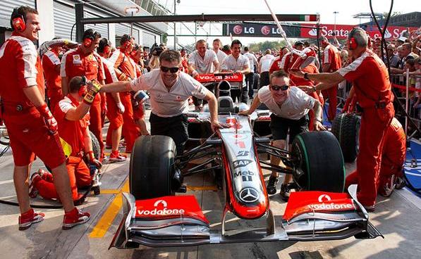 механики McLaren толкают болид Хэмилтона мимо механиков Ferrari