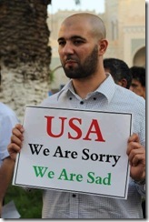 man holding sign that says - USA we are sorry We are sad in response to riots over anti muslim film