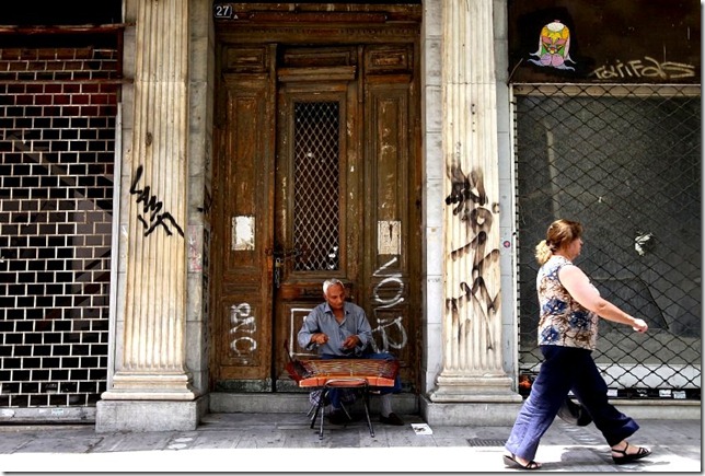 epa02812998 A woman walks past a street musician amidst closed shops in central Athens, Greece, 07 July 2011. Many shops in Athens' main shopping district have gone out of business amidst an economic crisis and recession. EPA/ORESTIS PANAGIOTOU +++(c) dpa - Bildfunk+++