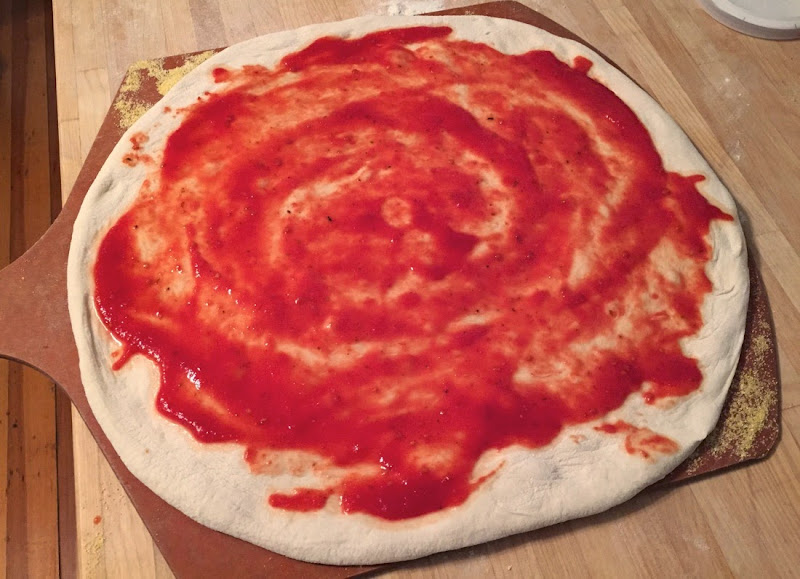 Image of pizza dough shaped and topped with sauce.