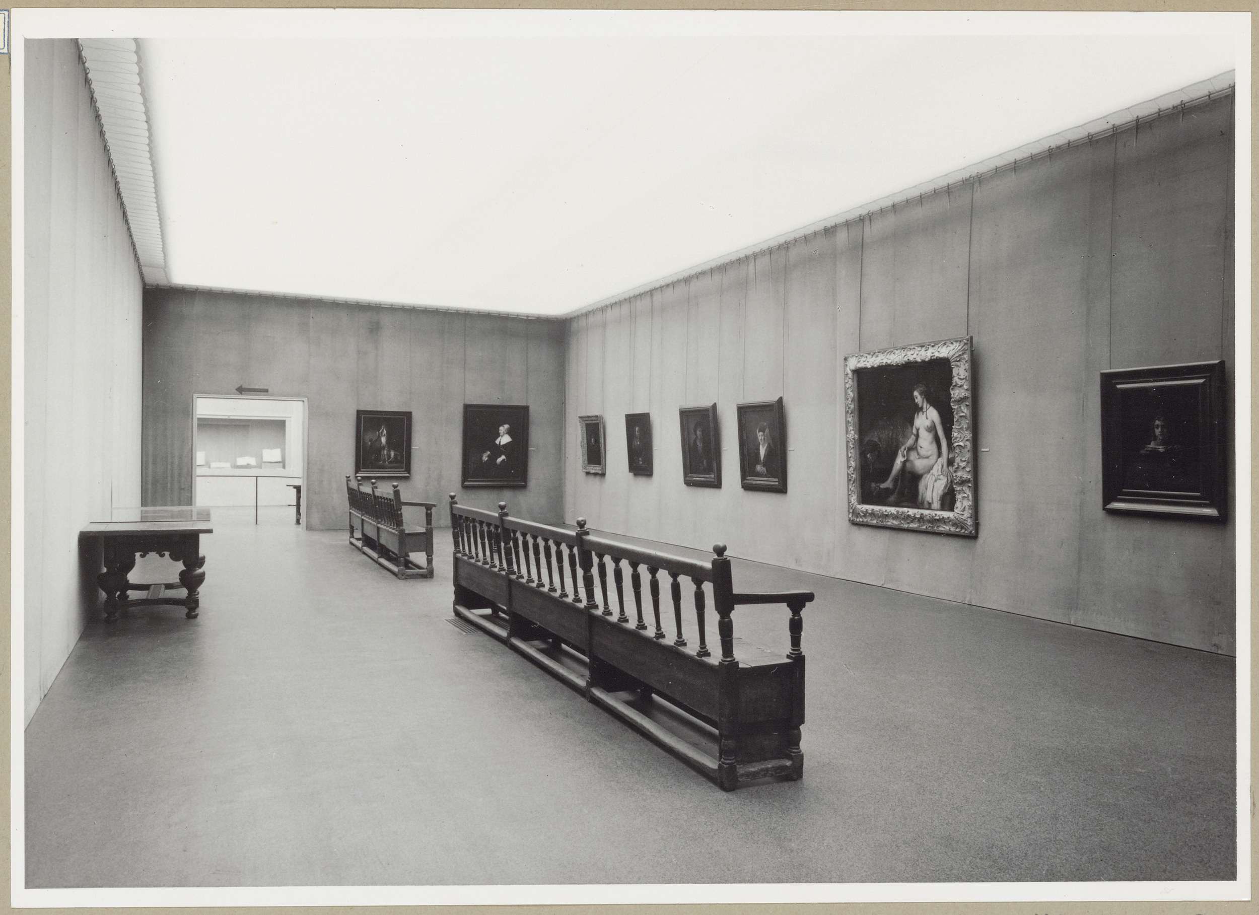 Zaal met acht schilderijen, links een tafel en achteraan een doorkijk naar manuscripten in een nis