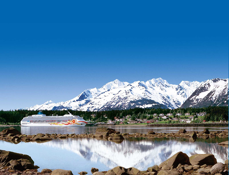 Norwegian Sun cruises along the Alaska coastline with a backdrop of snowcapped peaks and emerald green trees.